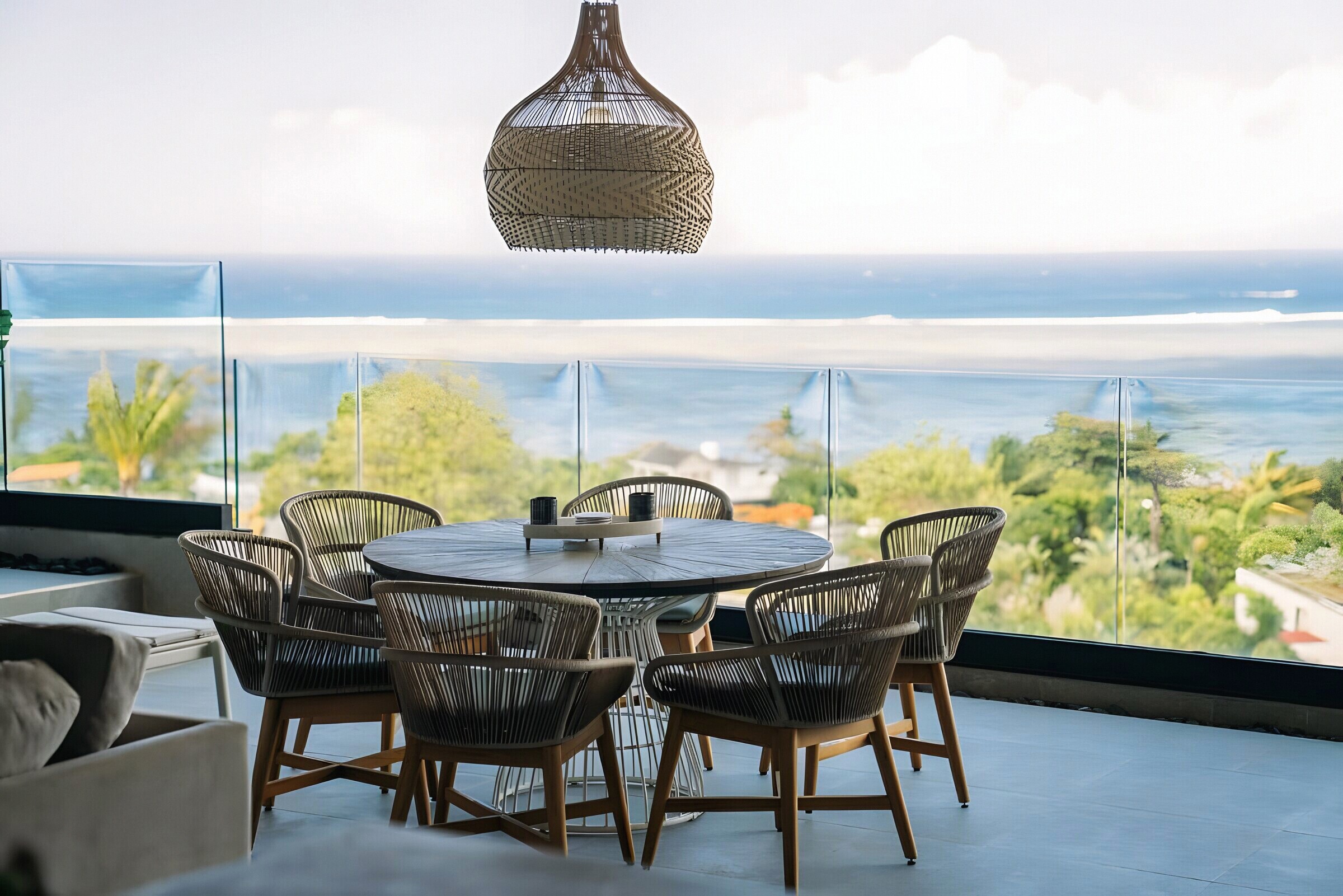 The terrace at The View — a round dining table under a rattan pendant, the lagoon and reef beyond the glass balustrade
