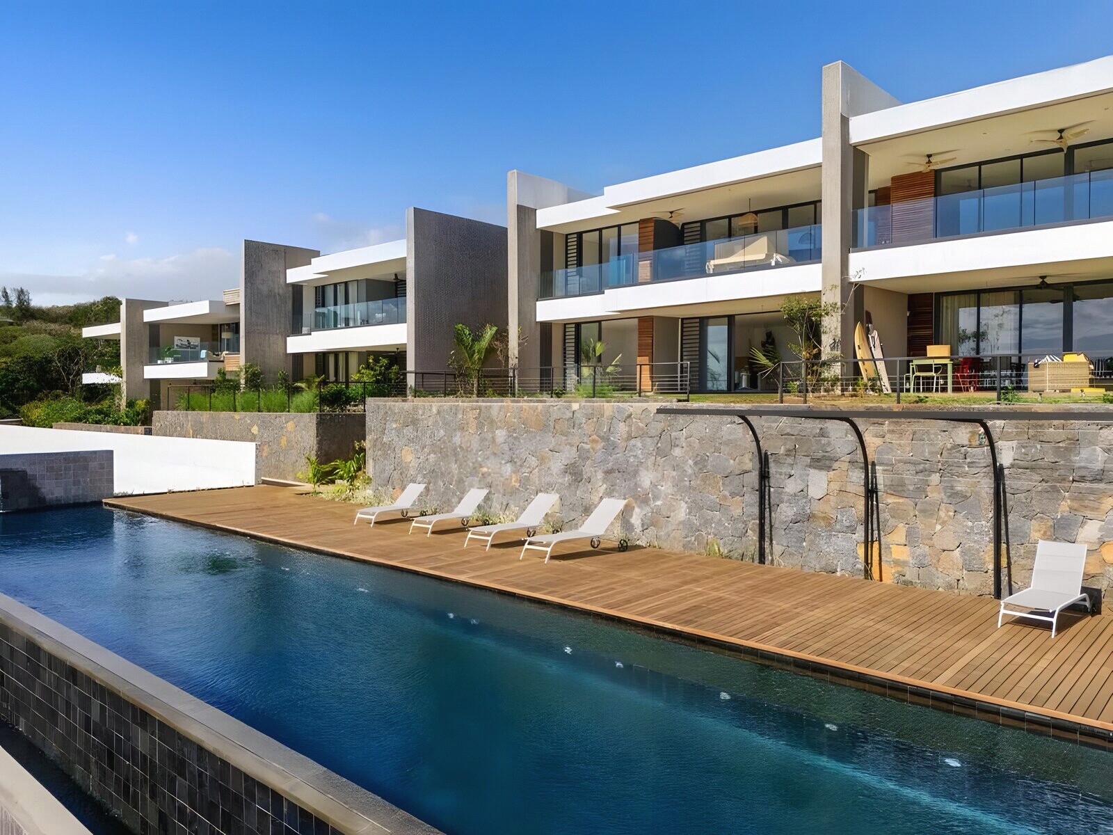The estate from the pool deck — teak boards, basalt wall and the long pool